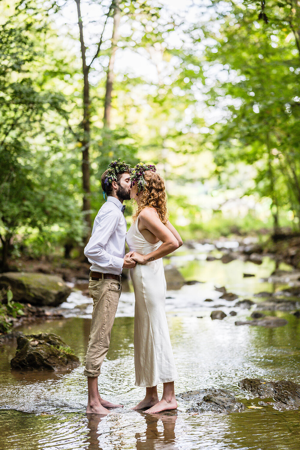 A couple on their elopement day stand in the shallow river at Fishburn Park in Roanoke, Virginia and kiss following their vow reading ceremony.