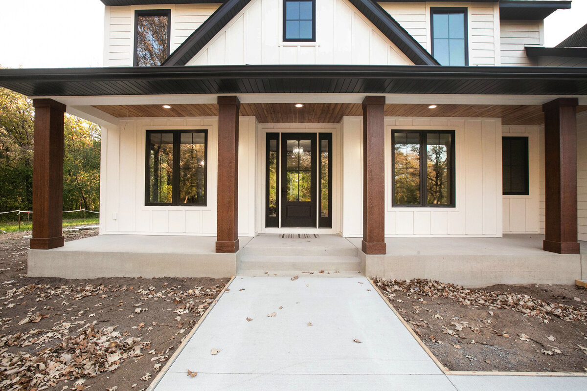 Exterior view of custom home in Big Lake Township, Minnesota with farmhouse details, cream siding, wood pillars and front porch built by Cornerstone Custom Builds