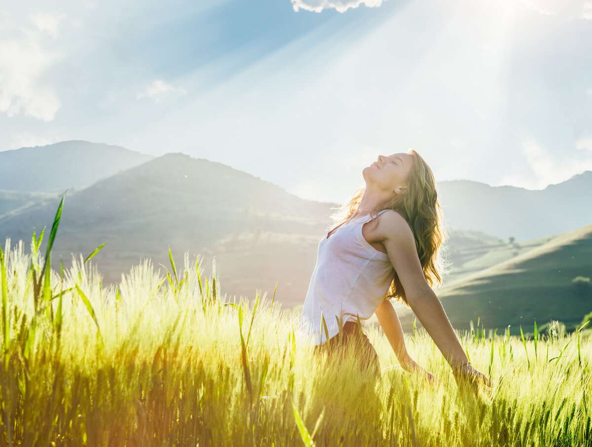 Woman sits in a field and looks up to the sky surrounded by mountains.