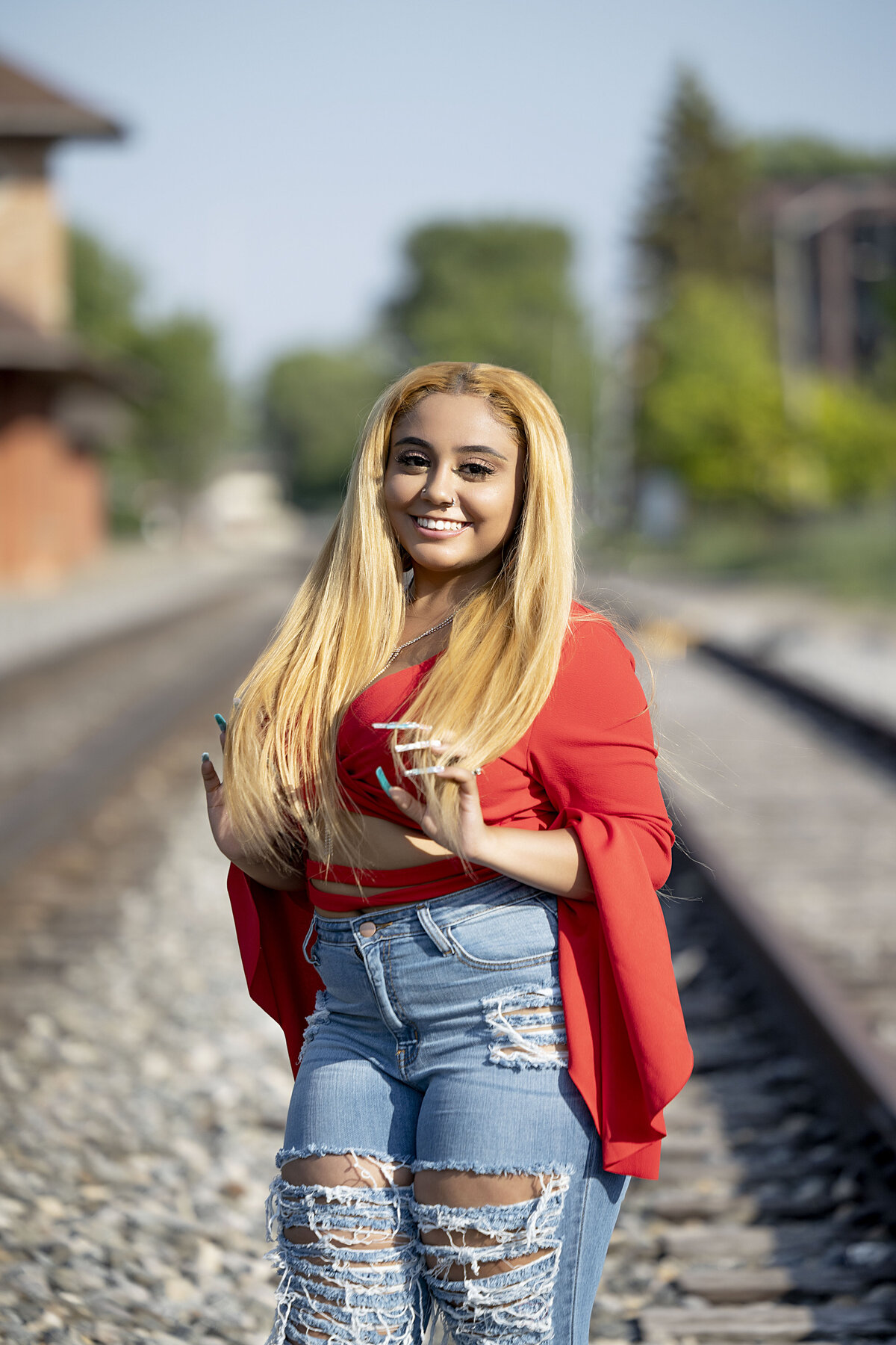 Ypsilanti Freight House Senior Photoshoot | Ypsilanti Michigan Senior Photographer, Senior girl in red top and destructed blue jeans holding hair on train tracks