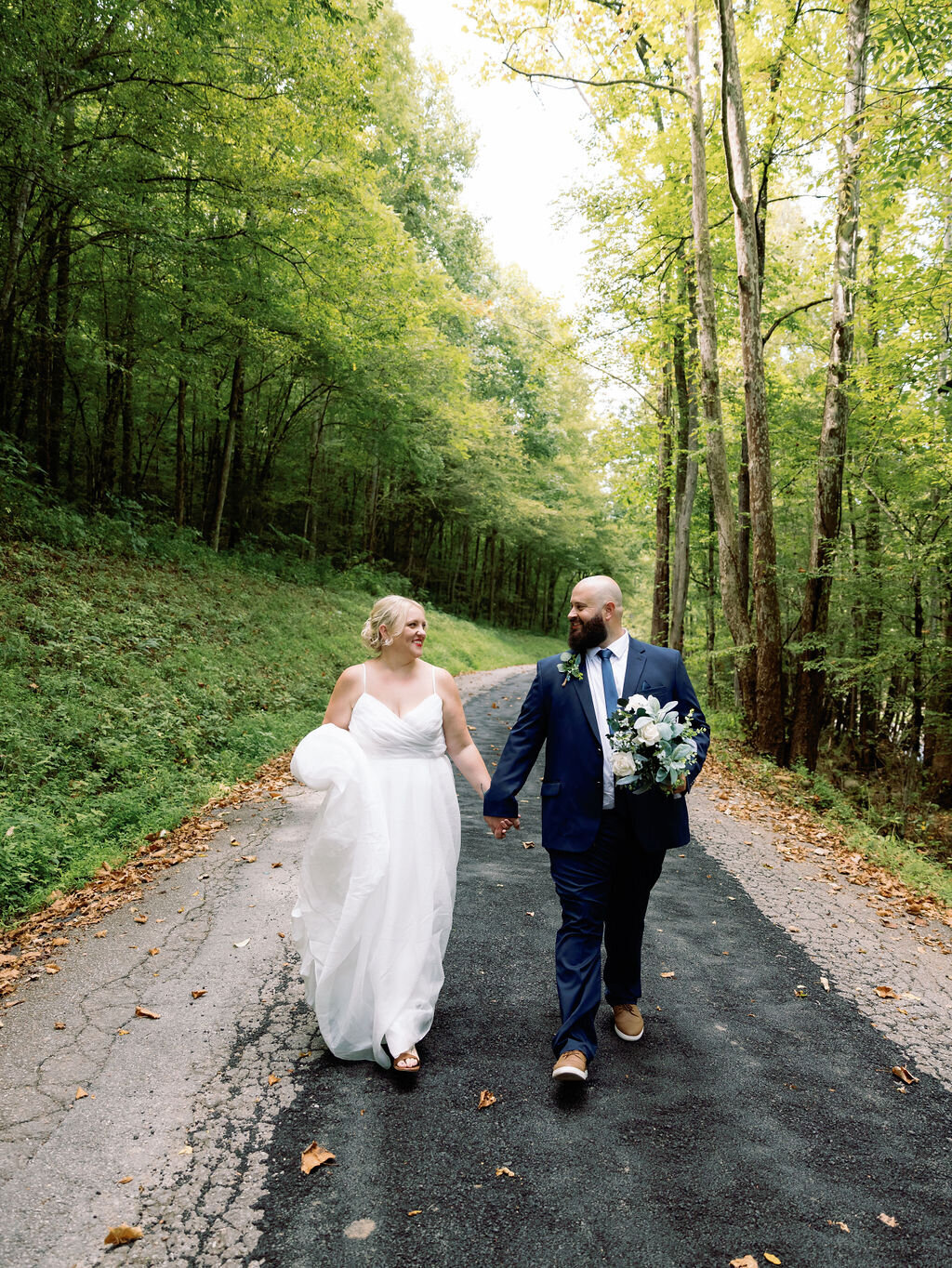 Gatlinburg elopement with couple holding hands and walking down a path surrounding by lush green trees at Greenbrier in the Smokies