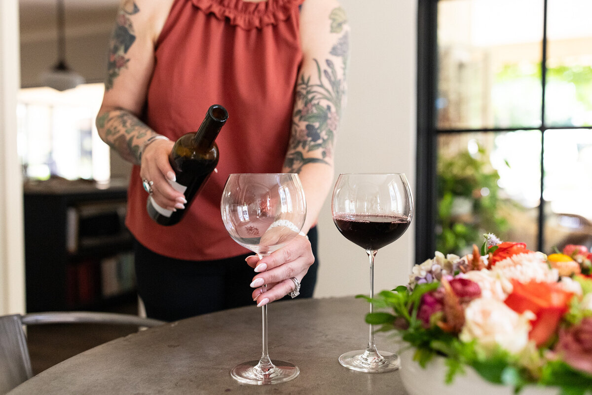 Female pours red wine into glasses for her branding photography photoshoot. 