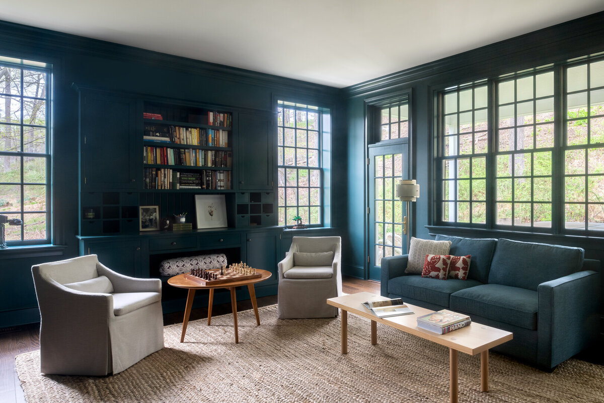 dark blue green living room with wooden chess table, coffee table, and armchairs