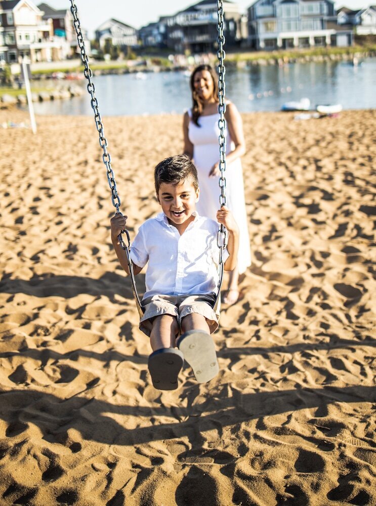 Mom in a white dress pushing her son on a swing 