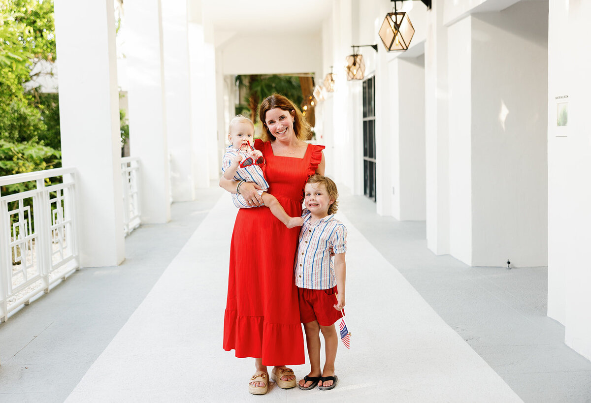 A mother in a red dress poses with her two children in a bright white hallway during a Florida Keys family session.