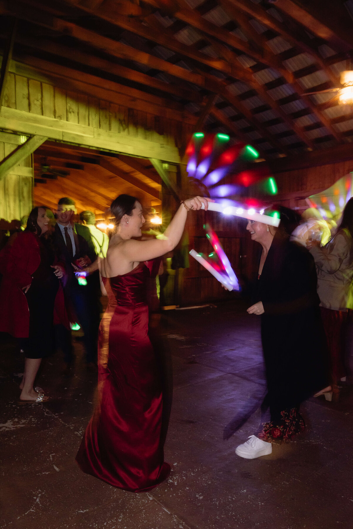 indoor wedding reception with bridesmaid in a red gown holding a light wand and dancing