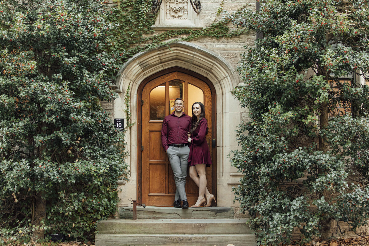 Couple posing by stone building doorway with green trees at Princeton University New Jersey