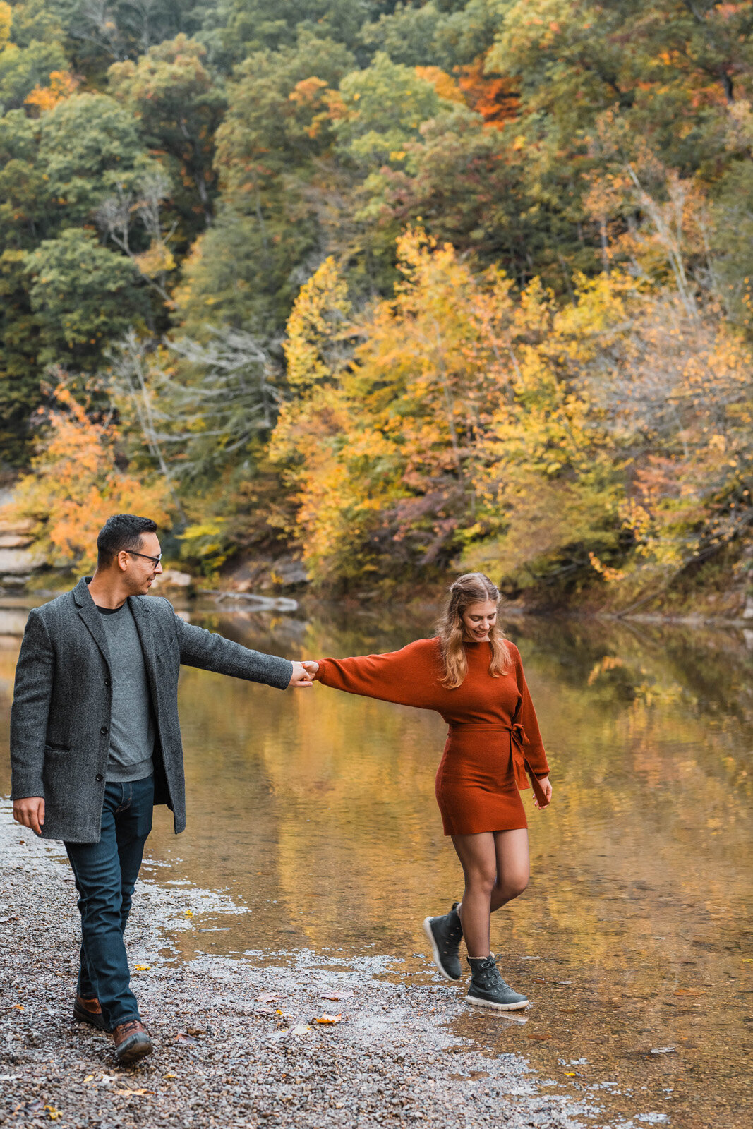 Engagement couple holds hands while walking in a stream