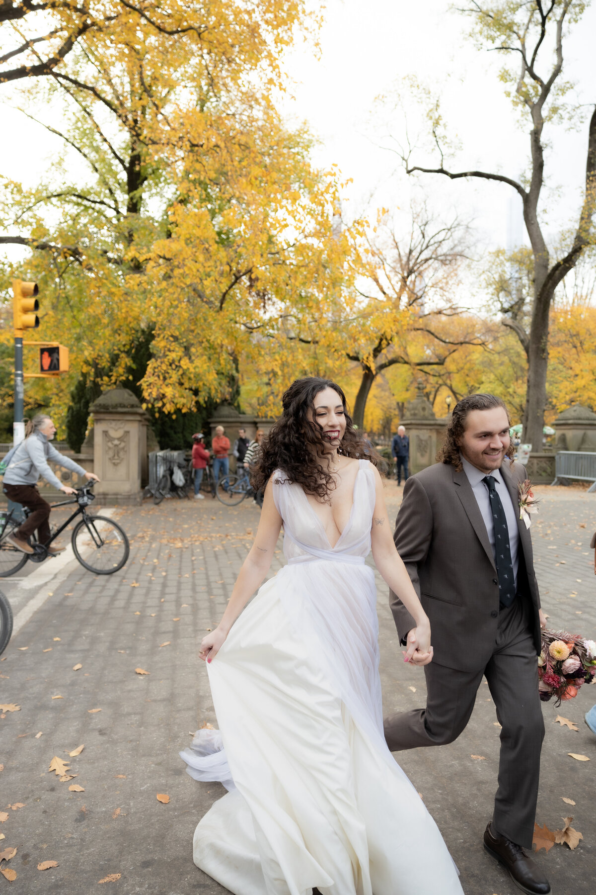 The bride laughing joyfully while holding her bouquet among autumn leaves in Central Park.