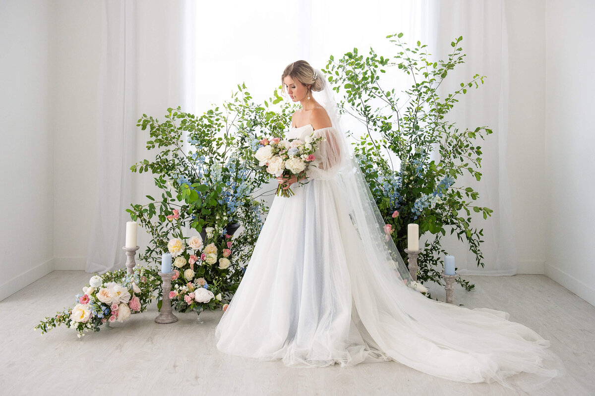 a full length photo of a bride standing at her ceremony site surrounded by blush, white and blue florals.  Captured by Ottawa wedding photographer JEMMAN Photography