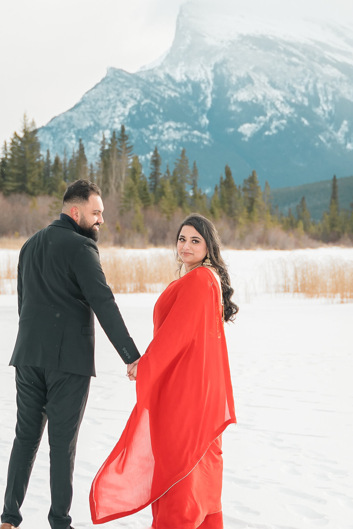 Couple walks hand in hand with snowy mountain backdrop during Banff engagement shoot.