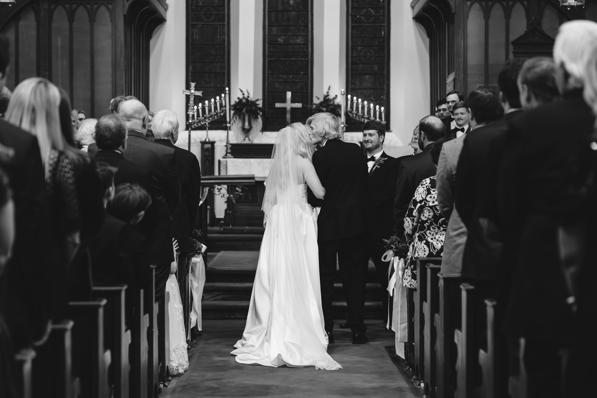 Father kissing bride's forehead before wedding ceremony.