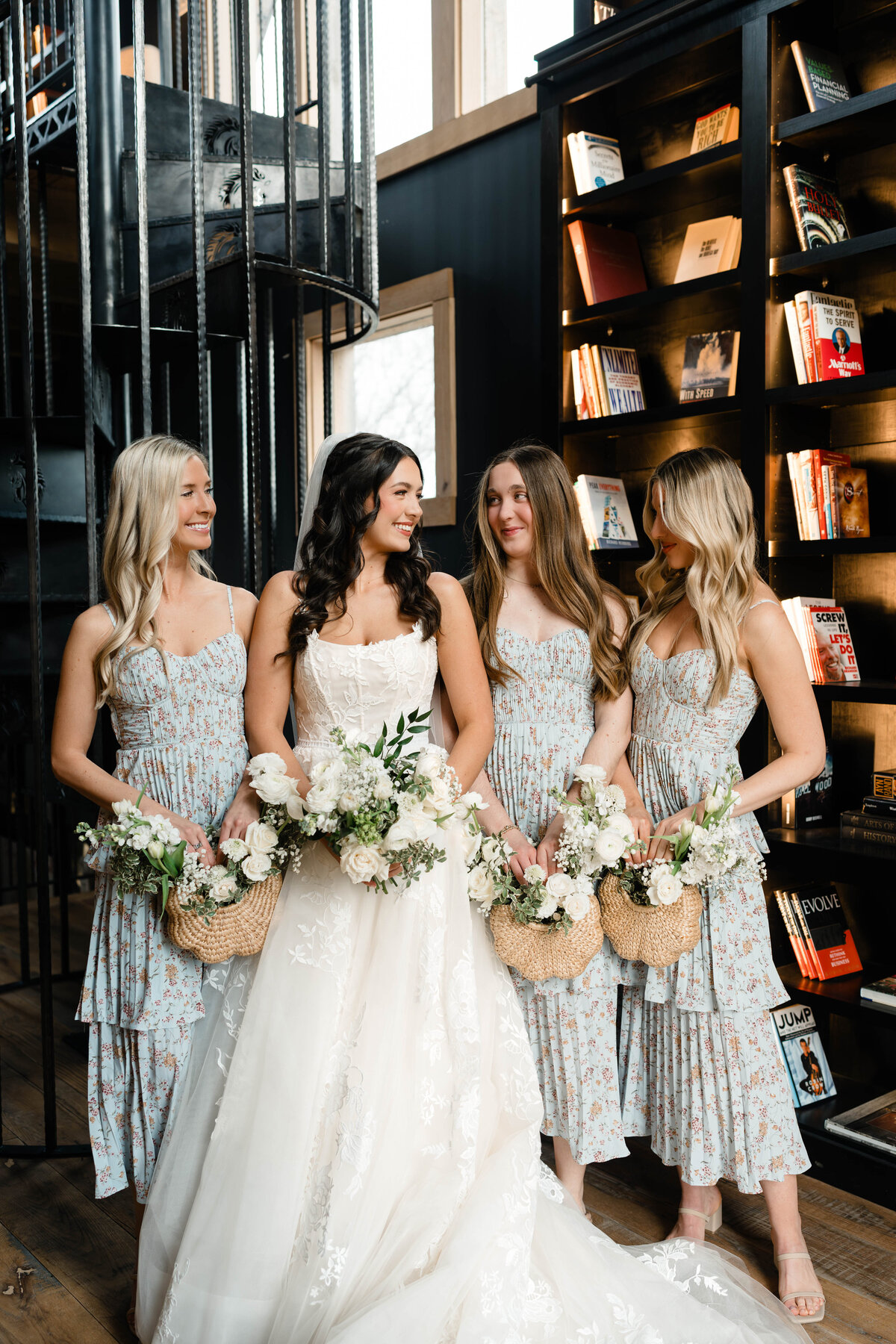 Bride smiling with her bridesmaids at a Franklin, TN wedding—holding woven floral baskets at Darkhorse Recording Studio with bookshelves and natural light.