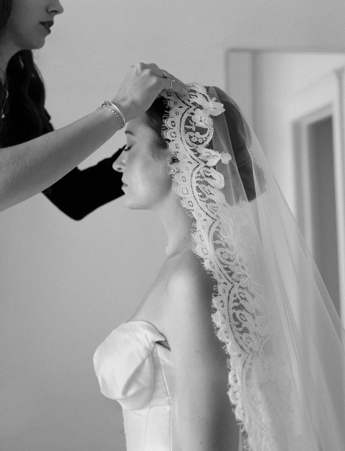 A bride's friend carefully places her lace mantilla veil before her unique Detroit wedding