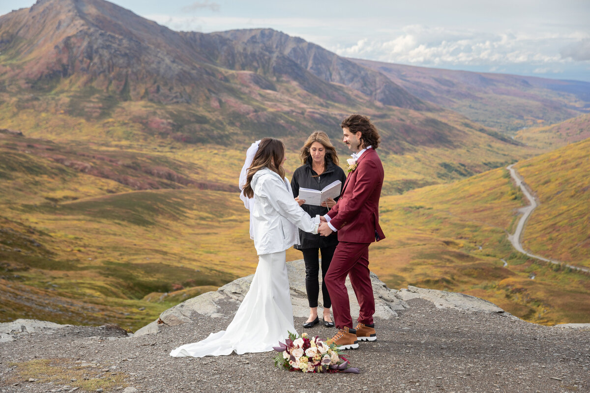 A bride and groom stand facing each other and holding hands as their officiant reads during their elopement ceremony.