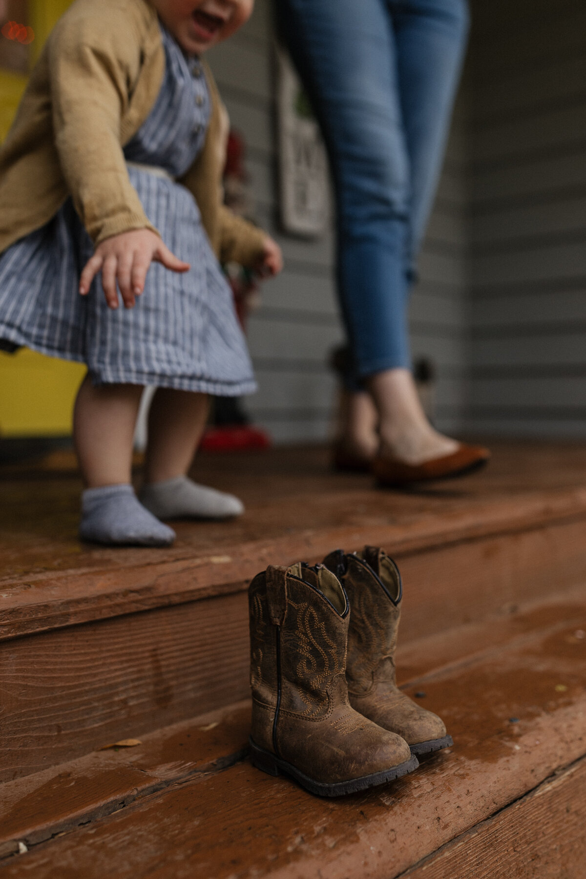 A close-up of tiny cowboy boots on a wooden porch, symbolizing childhood in a nostalgic and documentary family session.