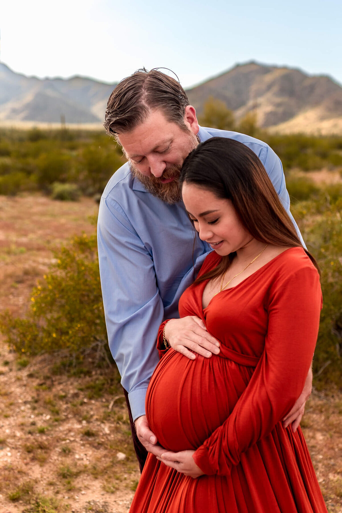 Expecting parents hugging while looking down sweetly at baby bump during Arizona maternity session