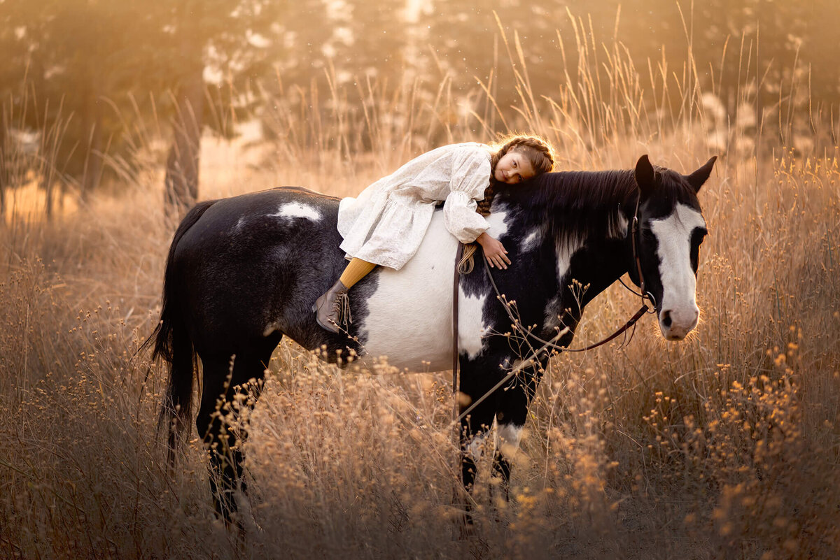 A little girl lays bareback on her horse at golden hour in Kamloops, BC. Taken by Brittany Danielle Photography