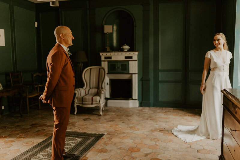 Papa en costume marron découvrant sa fille en tenue de mariée dans un chambre décorée à l'ancienne aux murs verts, et posant pour la séance photo mariage en vendée.