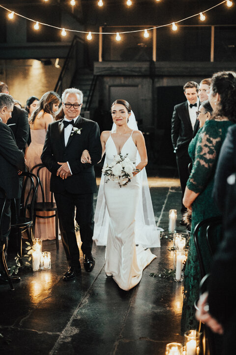 father and bride walking down the aisle under string lights
