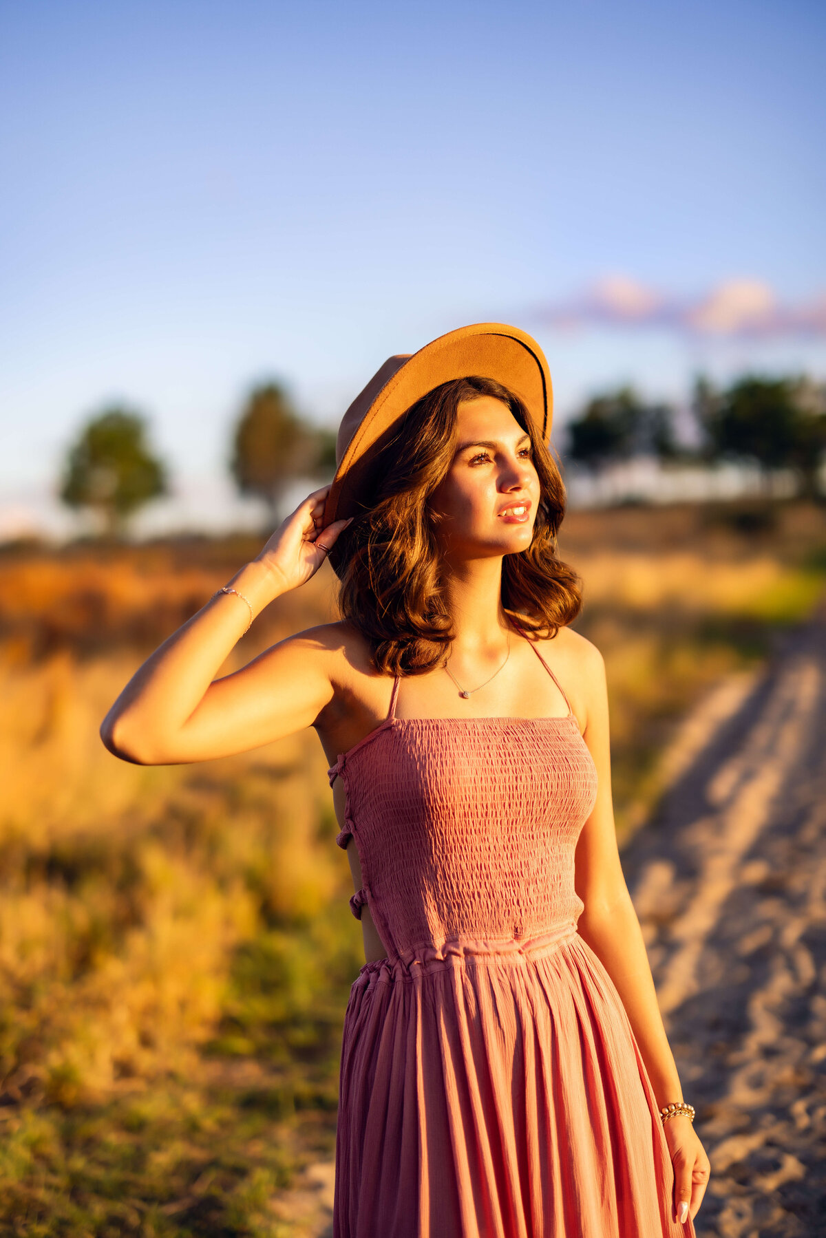 Golden hour senior session with beautiful girl staring directly into the sun with a beautiful soft expression in Winter Garden Florida along sandy path