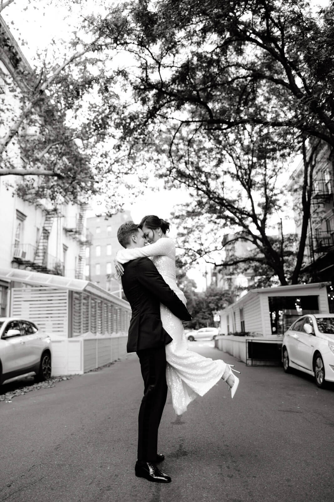 The groom is carrying the bride, touching heads, in the middle of a street in West Village, NYC. Image by Jenny Fu Studio