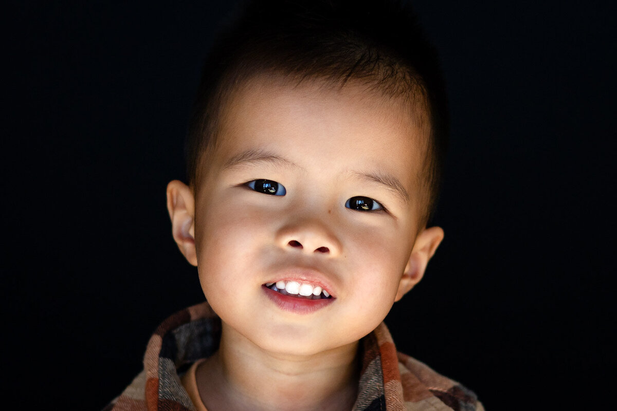 Smiling preschool boy in a plaid shirt against a dark backdrop during Bay Area School Photography session – Ellobelle Photography