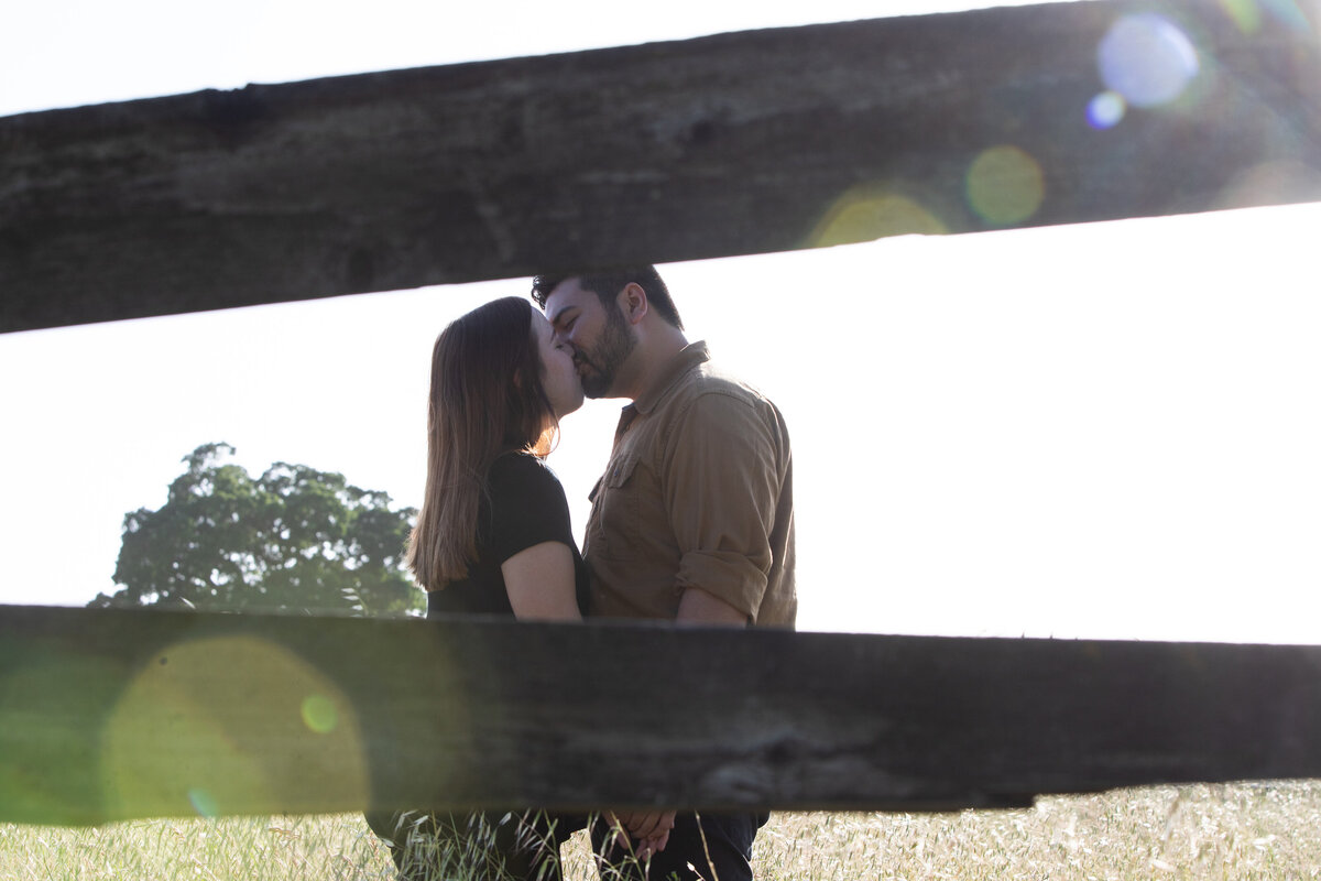 couple kissing between a fence