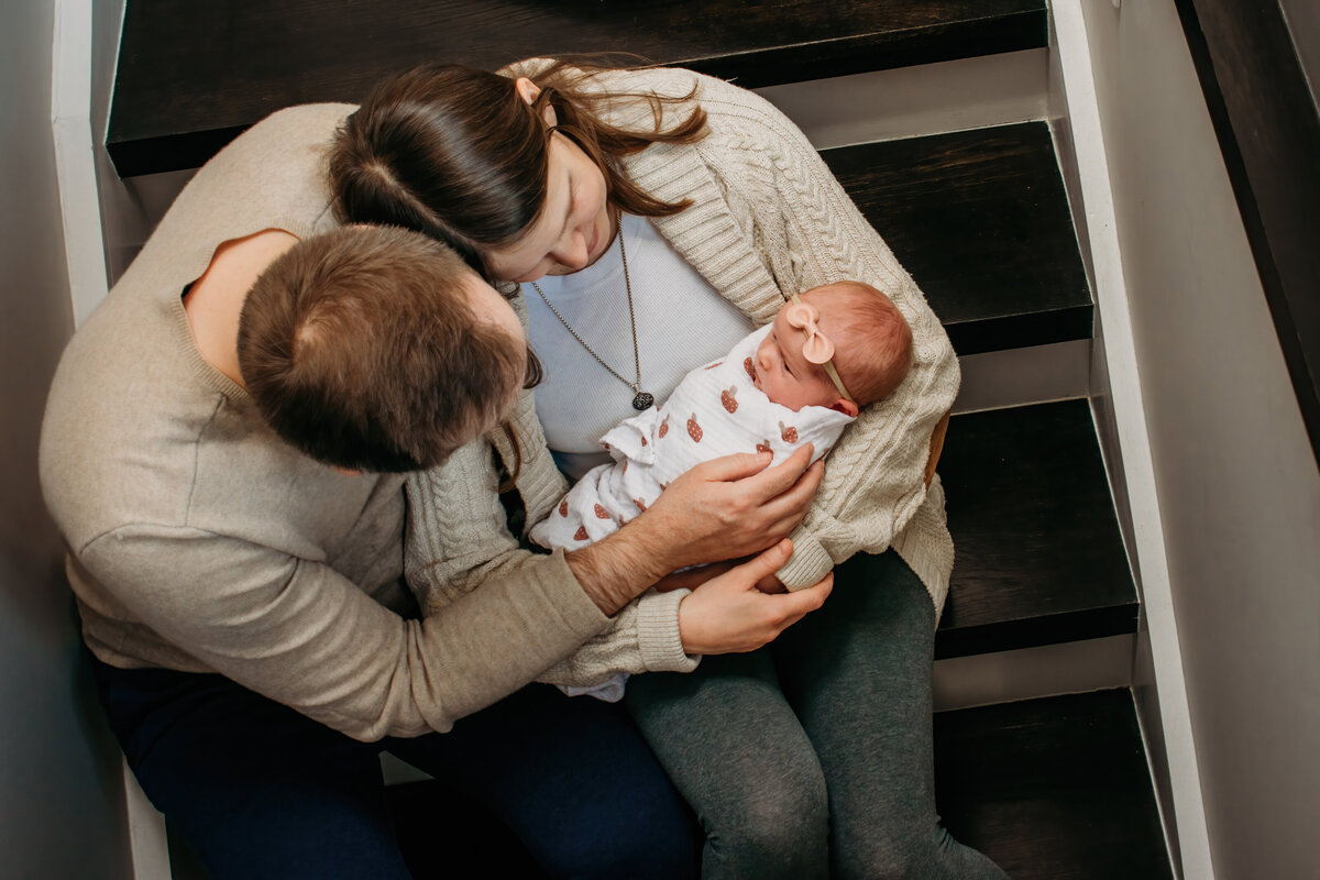 Candid photo of a family in their home on the stairs with baby girl during a newborn photoshoot in Chicago, IL