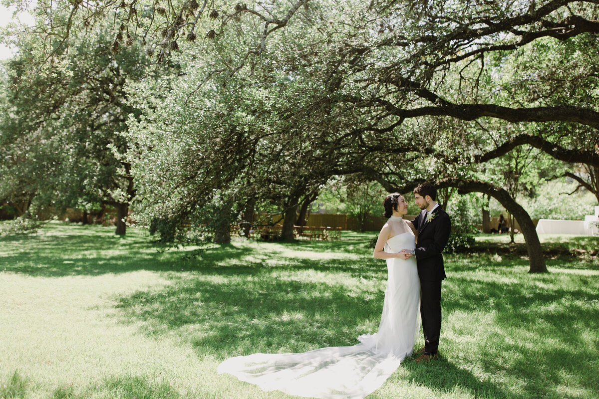 Bride and groom standing amongst trees in the grounds of Mattie's  Austin Wedding
