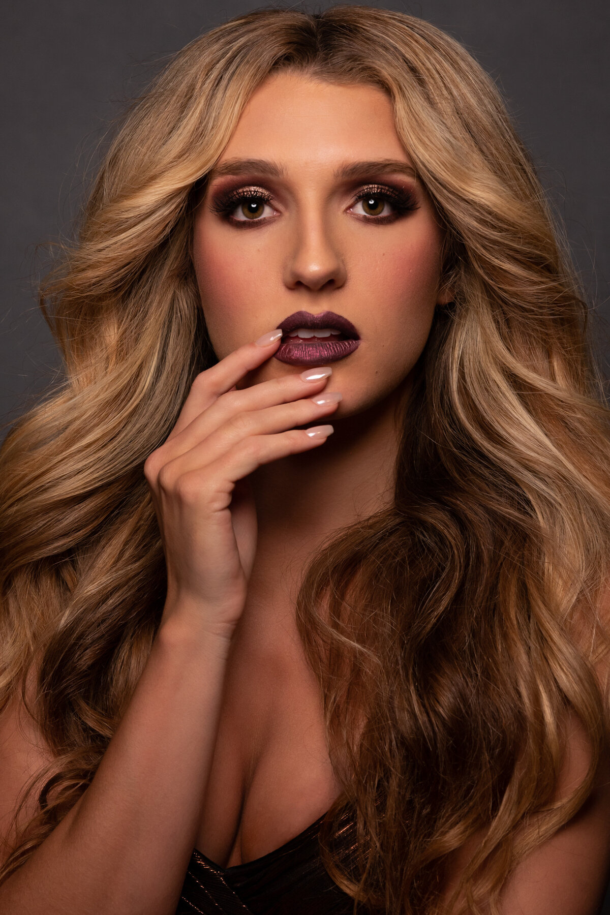 A close up of a blond woman with long curly hair touching her lips in a sexy way looking straight to the camera