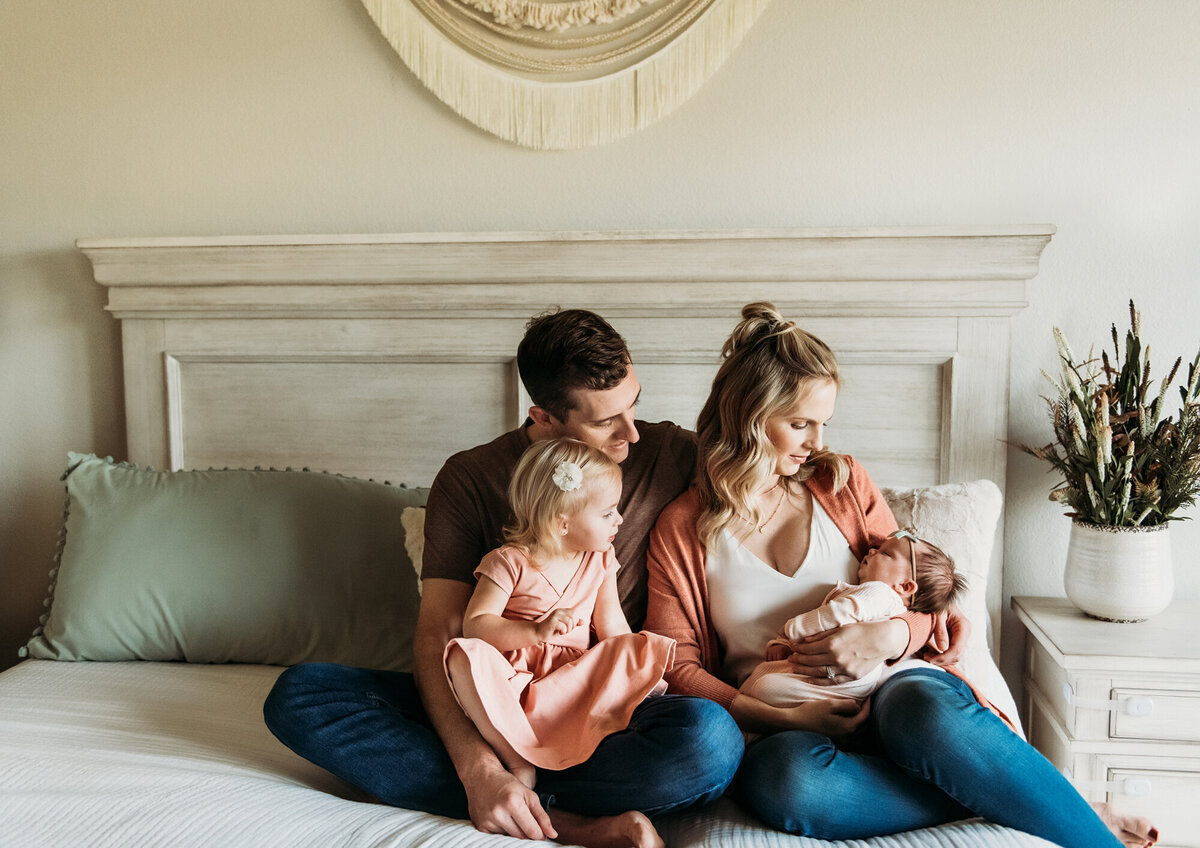 Newborn Photographer, Family of four snuggling new baby on the bed.