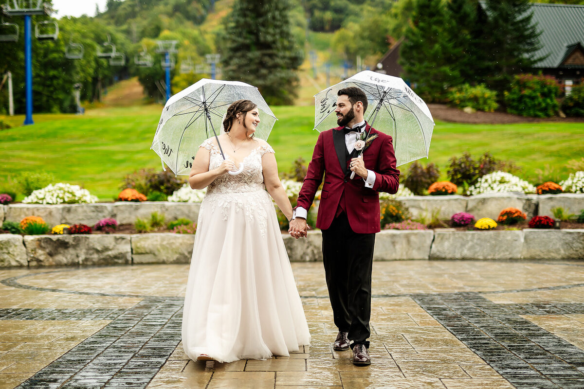 Bride and groom walking together with clear umbrellas at Pats Peak wedding venue in Henniker NH