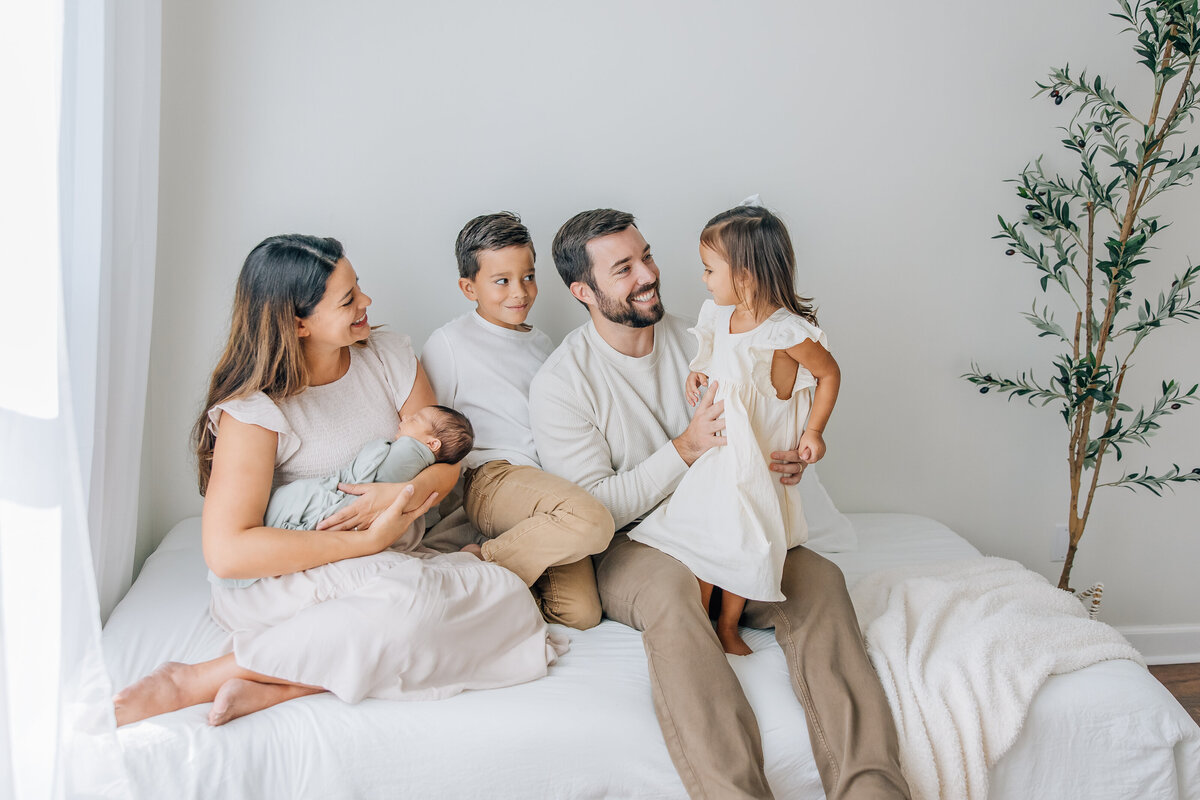 family of 5 sitting on bed with newborn baby