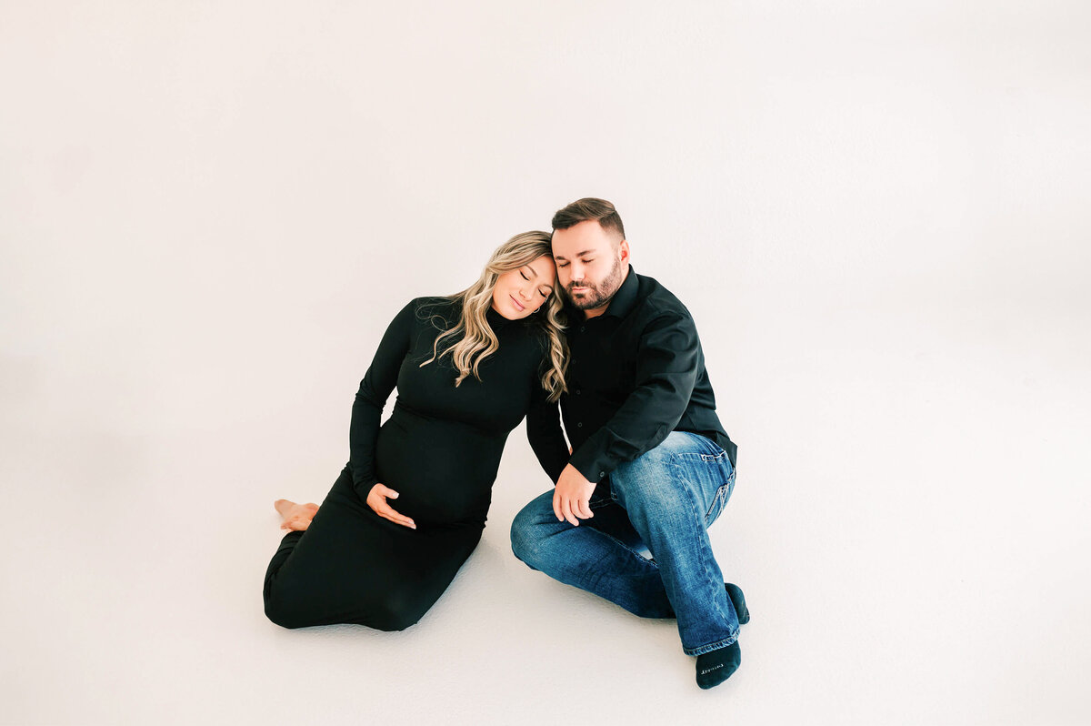 Springfield Mo maternity photographer captures pregnant couple sitting on white floor cuddling