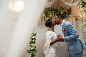 Bride and groom sharing first kiss under white floral arch during intimate St Augustine wedding ceremony with elegant drapery