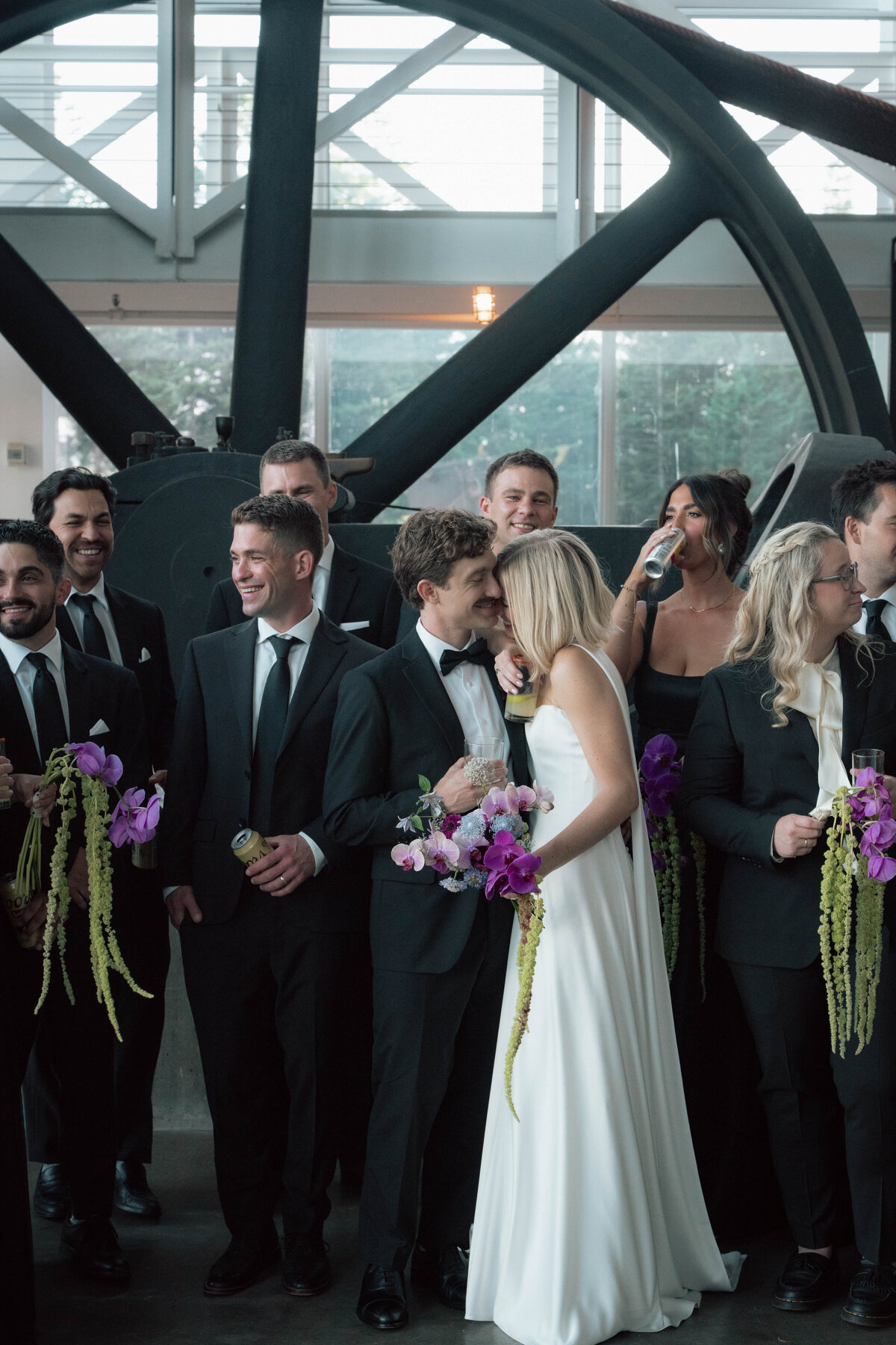 Wedding couple smiling with bridal party holding purple bouquets inside industrial venue