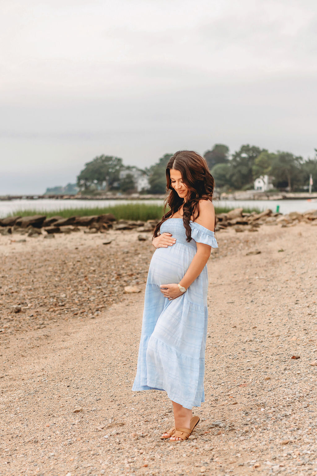 Connecticut maternity photographer captures pregnant woman in light blue dress on rocky coastal beach