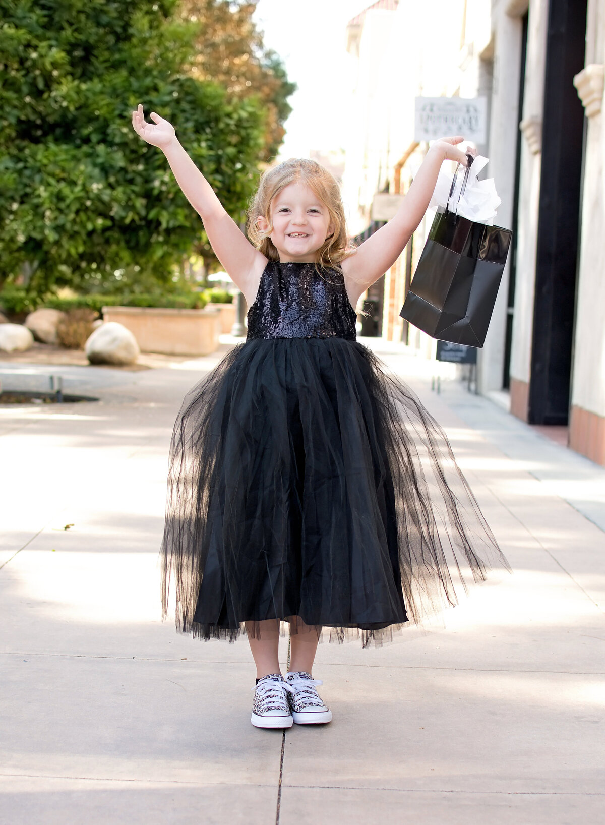 Lilttle girl in black dress holding black bag abover her head smiling
