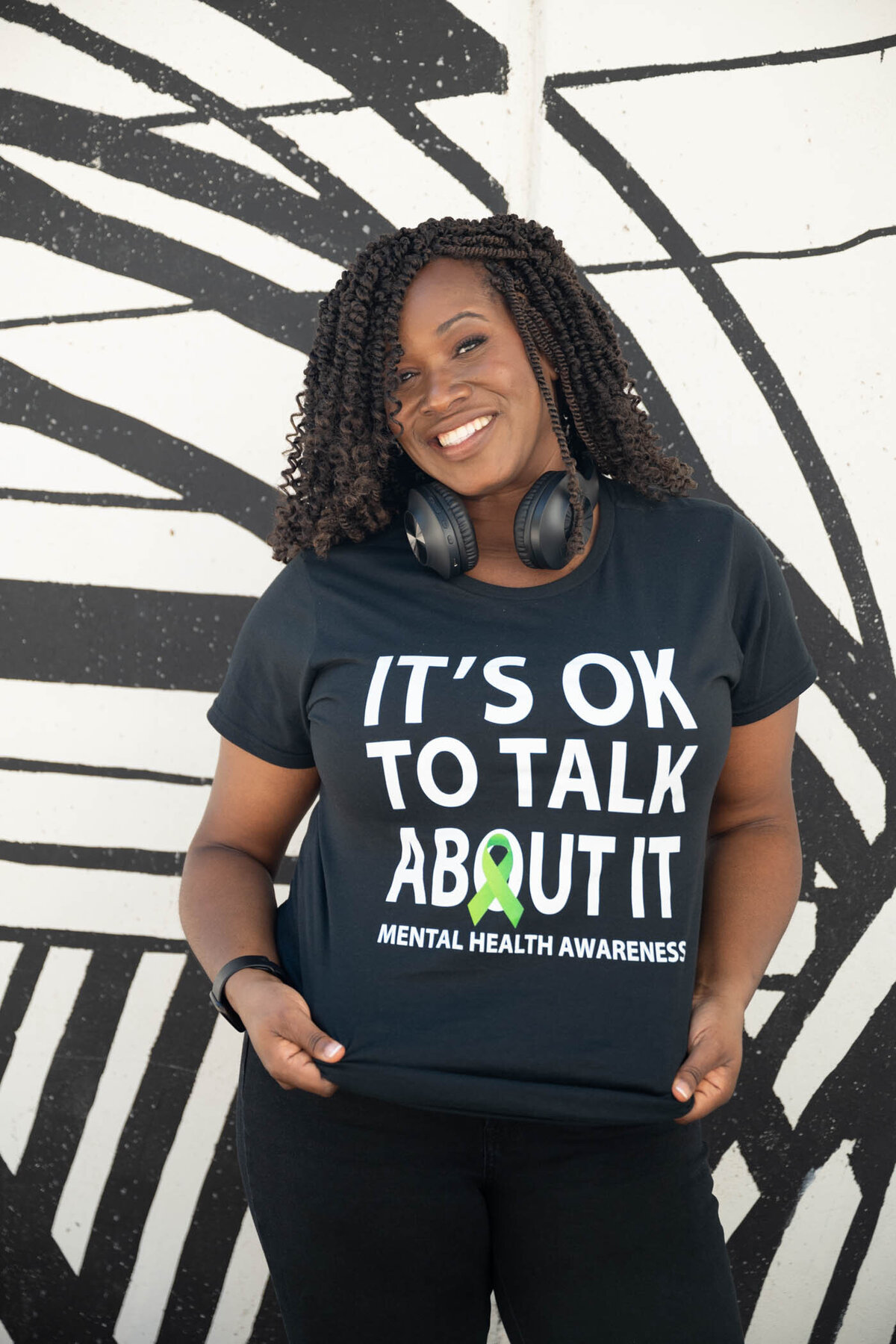 A portrait of a black woman wearing a t-shirt that says it's ok to talk about it