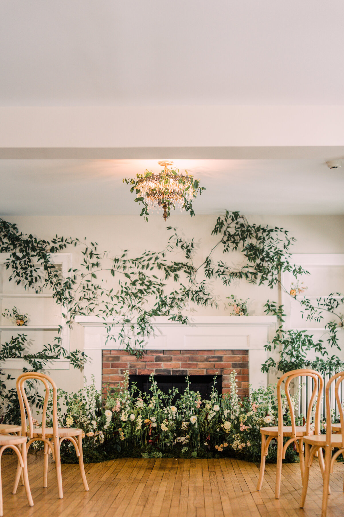 Room with white walls & brick fireplace covered in vines for wedding ceremony including garden nest & bentwood chairs at Cornman Farms