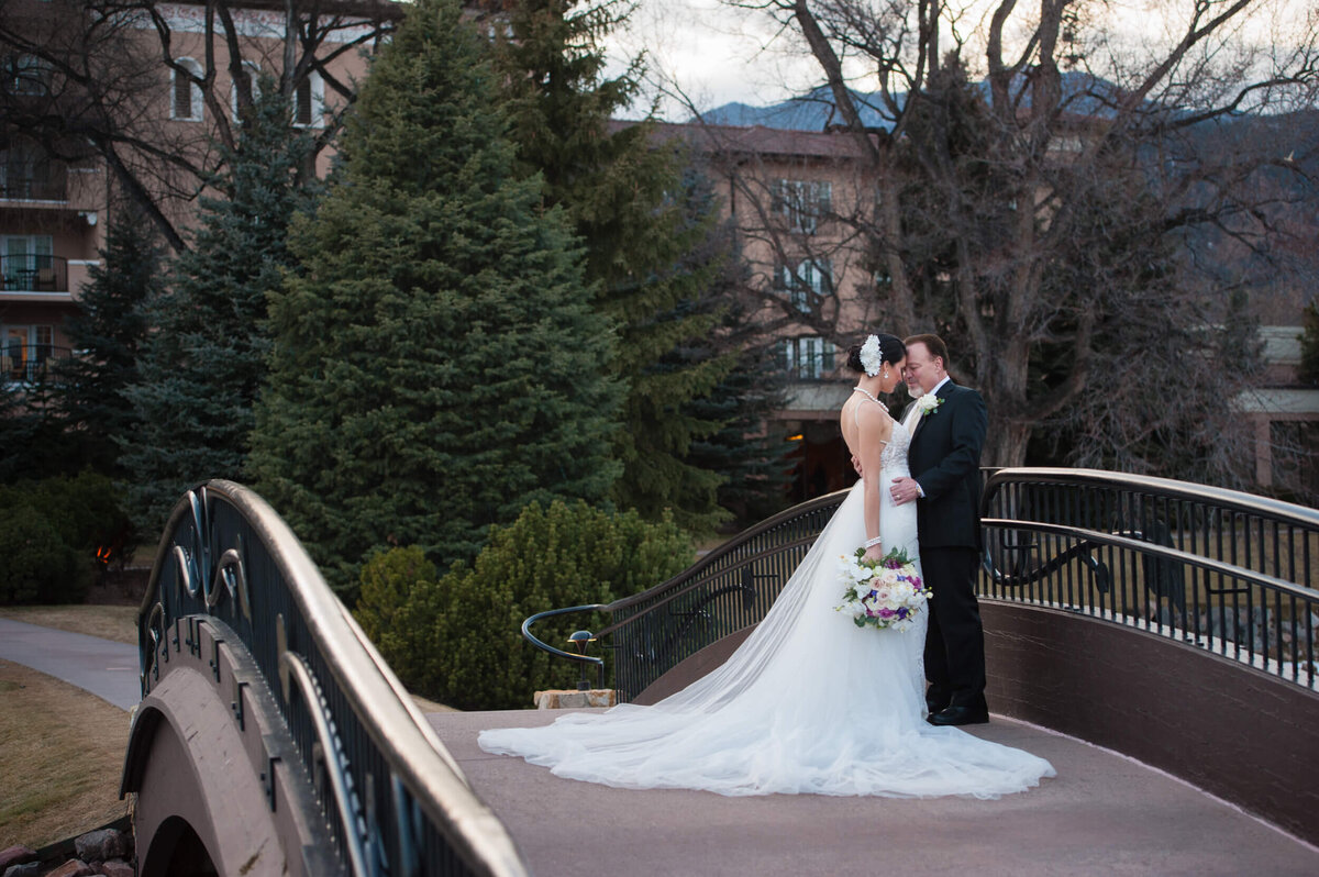 Bride and groom embrace each other while walking over the bridge at The Broadmoor