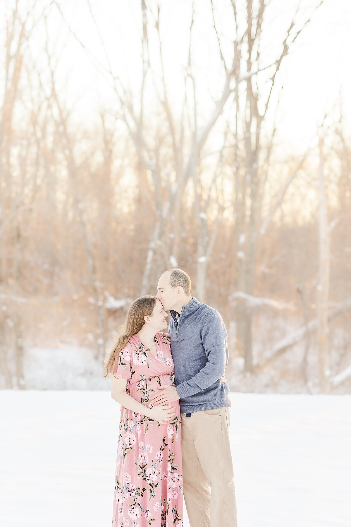 couple kisses during snowy winter maternity photo session with Sara Sniderman Photography in Medfield Massachusetts
