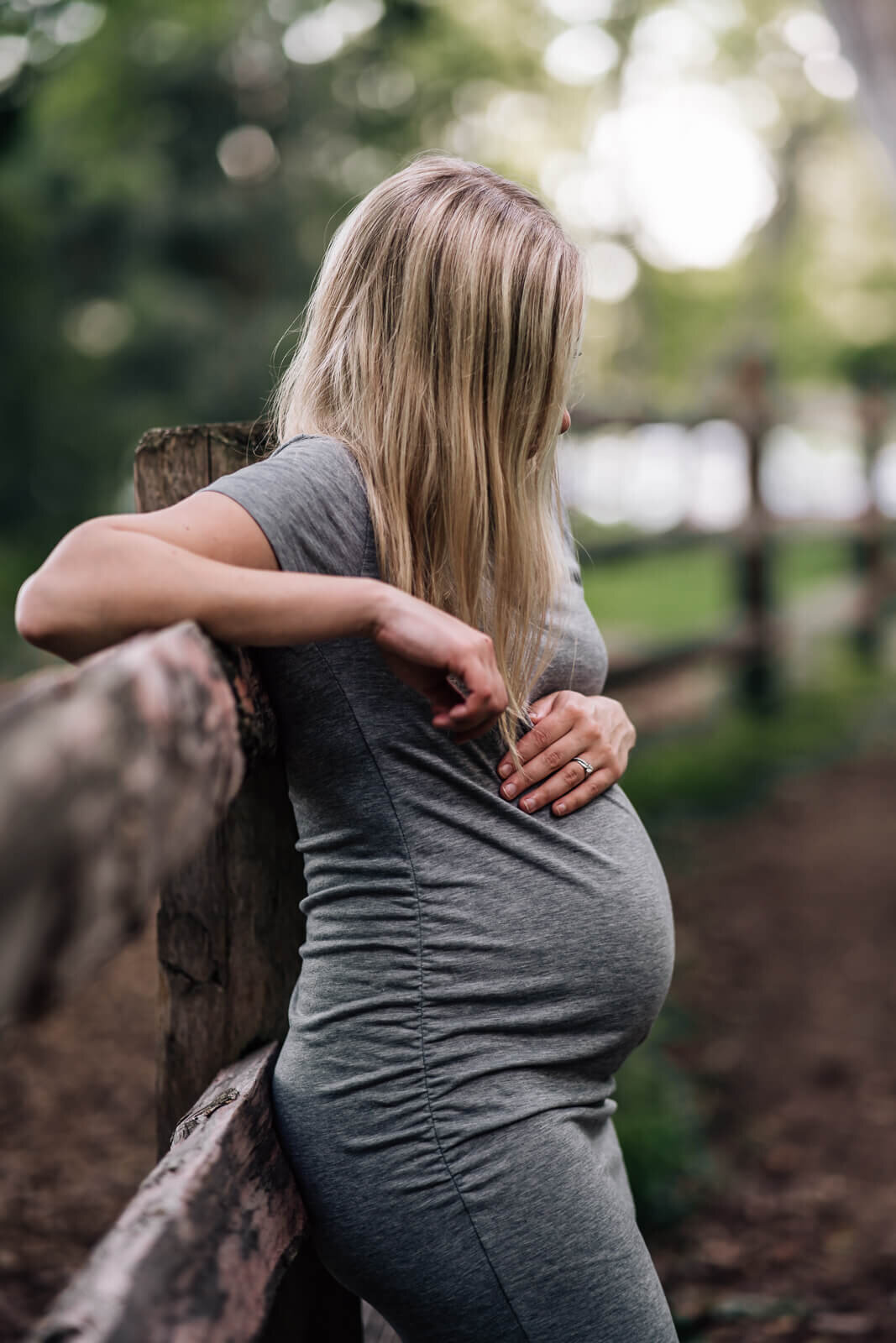 A pregnant mama, leans back on a fence and looks down towards her bump, while her long hair obscures her face.