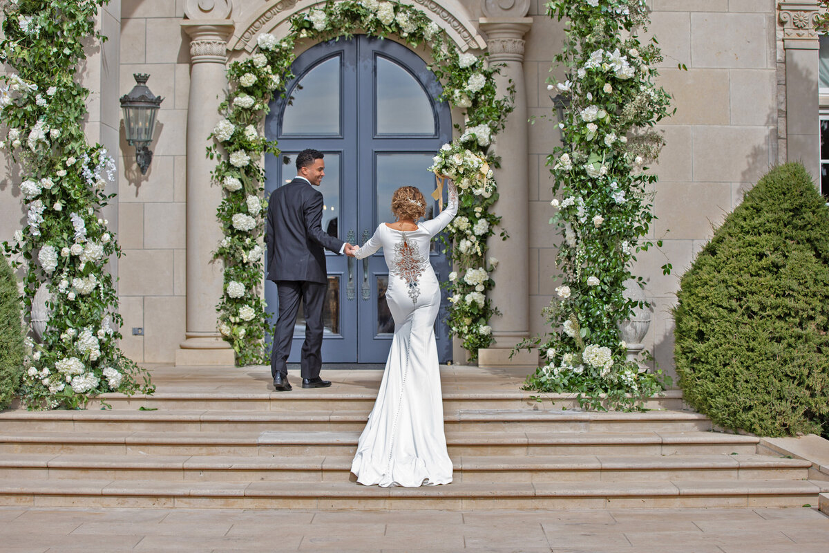 Bride raises her flowers in celebration as she and her groom walk into a building