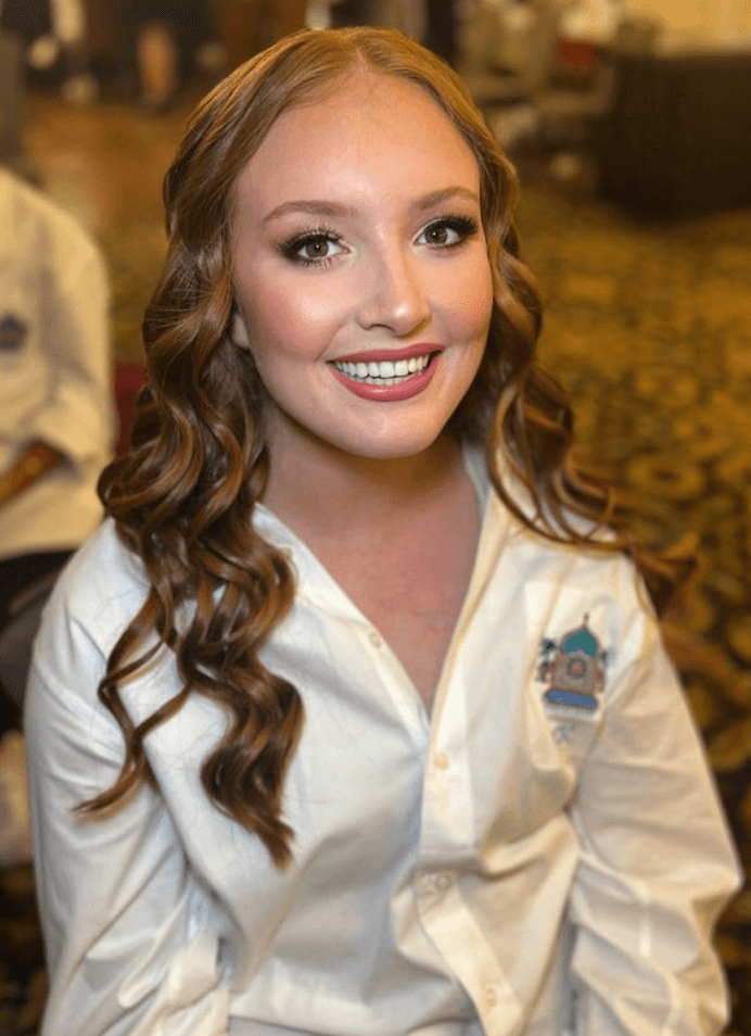 Young woman with curled hair and soft glam makeup smiling before a special event in Austin, styled by Mistique Makeup