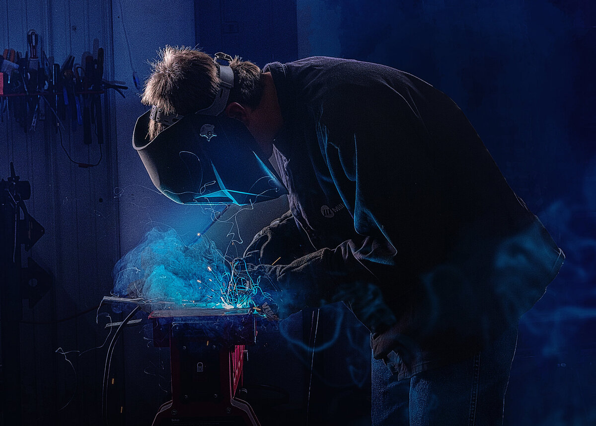 A high school grad welds under blue light in a shop captured by a Iowa Senior Photographer