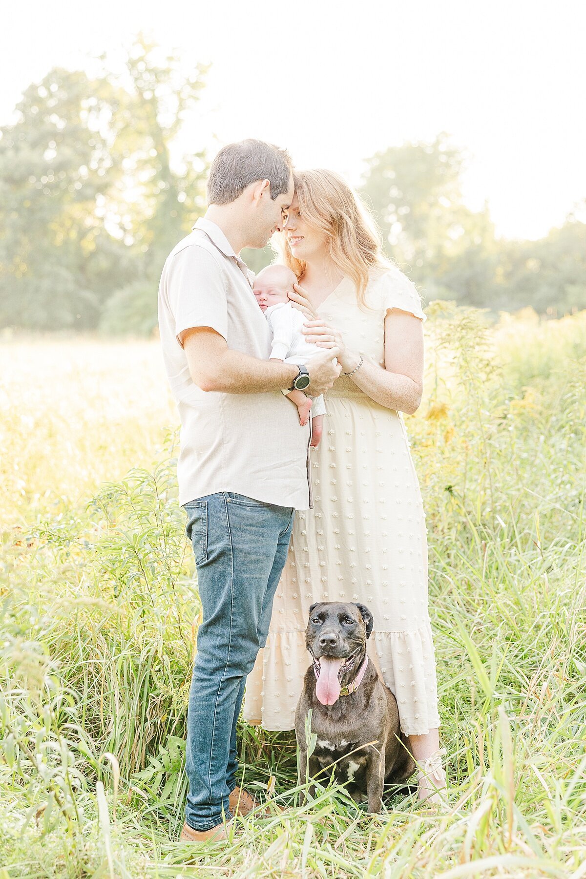 family stands with dog during outdoor newborn photo session at Heard Farm in Wayland Massachusetts with Sara Sniderman Photography