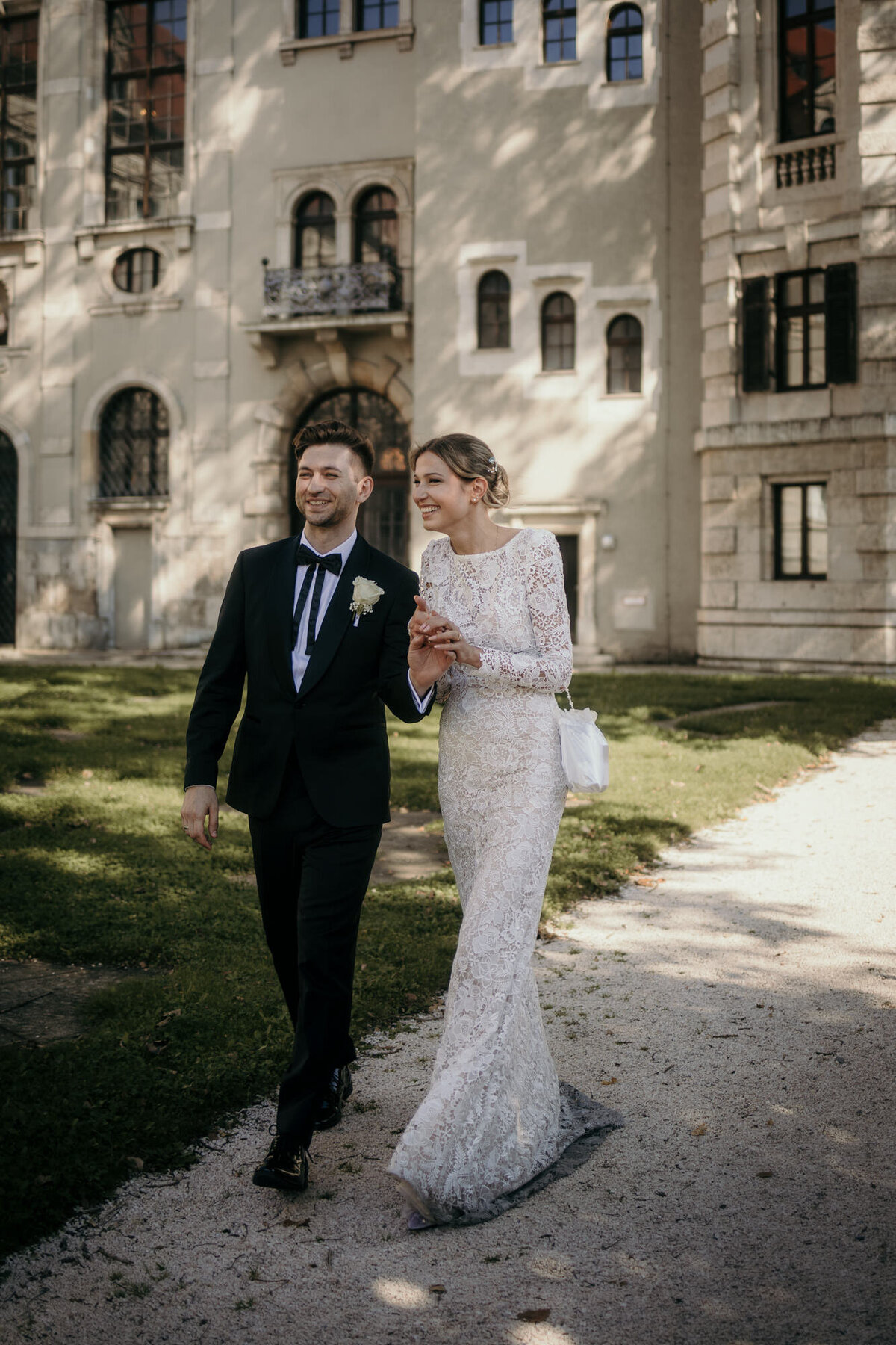 Newly weds walk in a courtyard, holding hands, smiling happily.