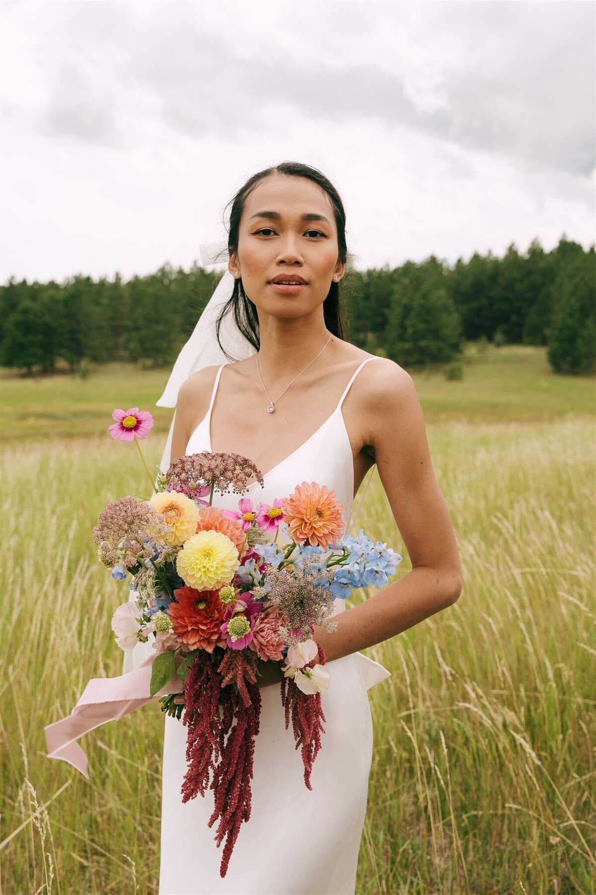 A bride holding a colorful floral bouquet looking at the camera. 